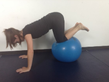 Photograph of a woman facing downwards with palms on the floor, and knees balancing on a blue inflatable ball