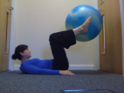 photograph of woman laying on her back on the floor with her head up, arms flat and legs up holding a large inflatable ball in between her ankles