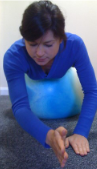 Photograph of a woman laying facing downward balancing her tummy on an inflatable ball. On palm is placed down, the other is raised in front of her