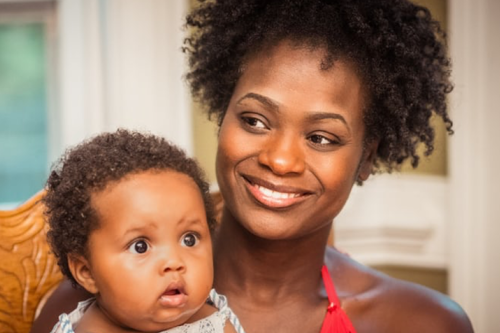 Photograph of mother holding her baby on her lap, both smiling towards the camera.