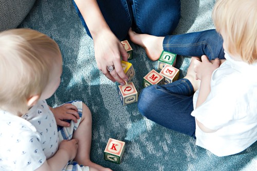 Photograph of two children sitting on the floor with building blocks with letters on them about to play.