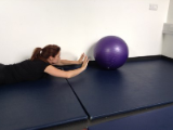photograph of a woman laying on the floor on her front reaching ahead to tap or push a purple inflatable ball