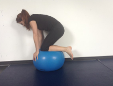 woman kneeling on an inflatable ball with back arched downwards and hands holding onto the ball