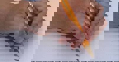 Yellow pencil grasped between the tips of the thumb, index and middle finger of a child's hand